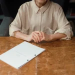 Cuaderno abierto con pluma sobre páginas en blanco, rodeado de libros apilados en escritorio