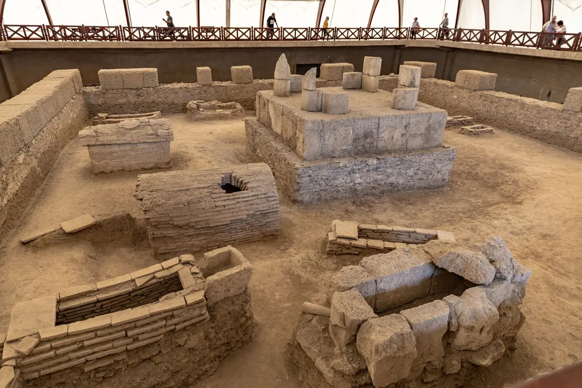 Arqueólogos trabajando en una excavación arqueológica en un sitio antiguo con estructuras de piedra y capas de tierra.