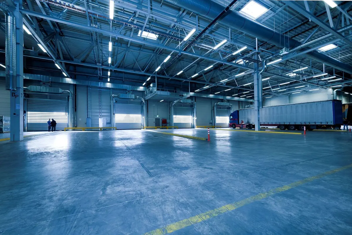 Interior de hangar industrial amplio con estructura de acero y espacios abiertos para construcción de escenarios