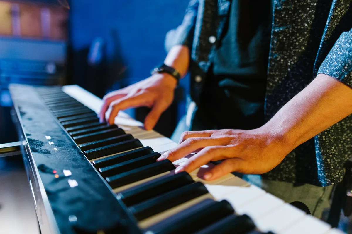 Manos de pianista sobre teclas de piano con partituras y luces de escena de fondo
