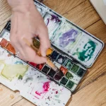 Artista trabajando con materiales experimentales en su estudio, rodeada de objetos vibrantes y bocetos creativos