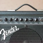 Escenario vacío con micrófono vintage, guitarra apoyada y amplificador, ambiente de camerino