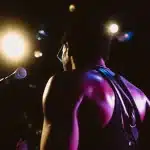 Músico con guitarra en el escenario ante una audiencia atenta bajo luces cálidas