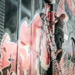 Manos y siluetas junto a un mural en proceso frente a un centro cultural