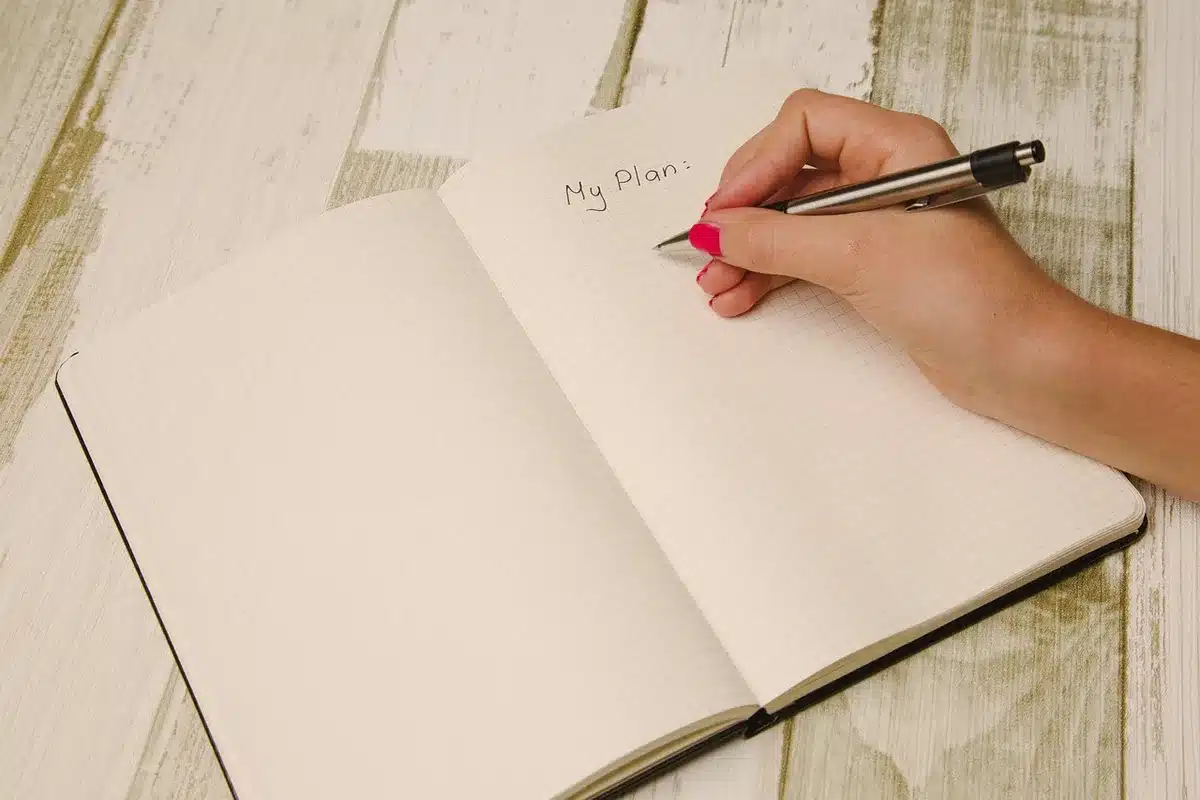 Manos anónimas hojeando un manuscrito sobre una mesa de café, junto a un bolígrafo y libros desenfocados
