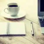Mesa de trabajo con cuadernos, manos anónimas y un portátil apagado