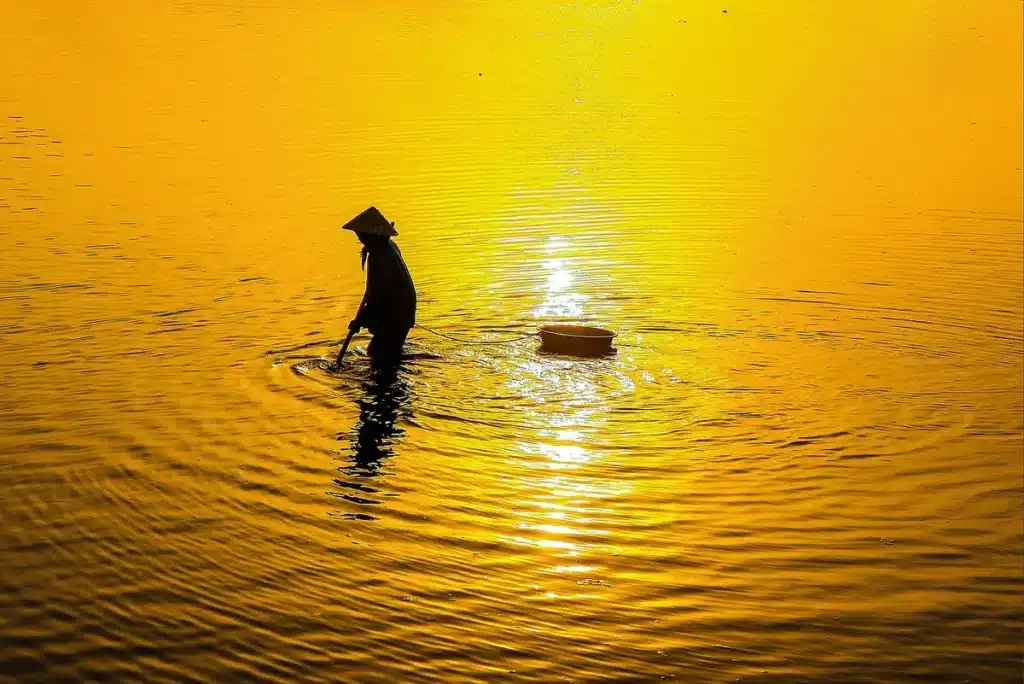 Manos con cañas frente a embarcaciones en el río Paraná al atardecer