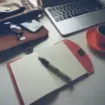Periodista joven con libreta, bolígrafo y grabadora sobre mesa con recortes